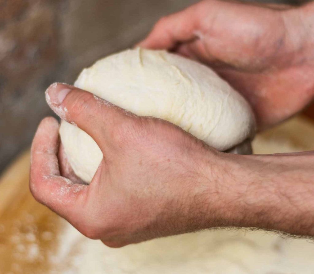 Pizza maker hands kneading a pizza dough dusted with flour